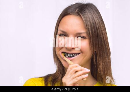 Close-up of happy woman brushing teeth with eco friendly bamboo toothbrush with black charcoal whitening toothpaste. Stock Photo