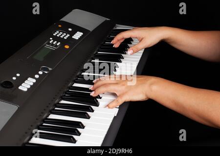 close-up of female hands pressing keys on an electronic synthesizer or piano, isolated on a black background Stock Photo