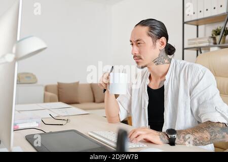 Pensive frowning freelancer drinking cup of coffee when working on big project for client Stock Photo