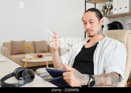 Portrait of pensive graphic designer with stylus and table computer in hands working on company logo Stock Photo