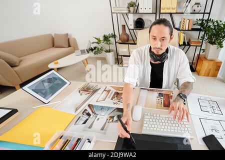 Professional designer working on interior design of big house for client, he is sitting at table with plans and photos Stock Photo