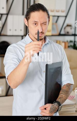 Graphic designer closing one eye and looking at tip of digital pen in his hand Stock Photo