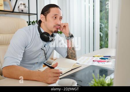 Pensive bored graphic designer reading brief from client and figuring out what he should draw Stock Photo
