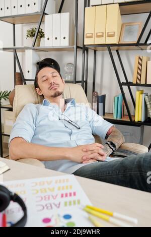 Graphic designer sleeping in chair at his home office when having short break after working on company logo for client Stock Photo