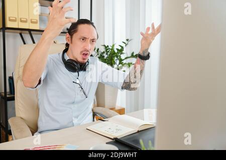 Angry indignant graphic designer actively gesturing after reading e-mail from client asking for a few changes Stock Photo