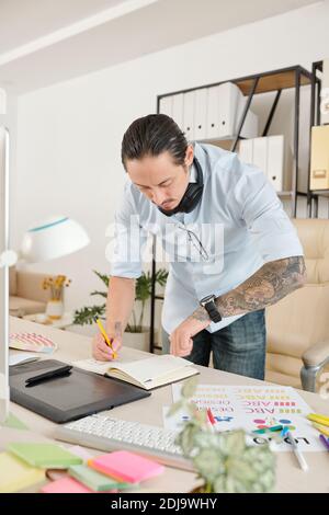 Freelance graphic designer checking time on is wrist watch when taking notes in planner Stock Photo