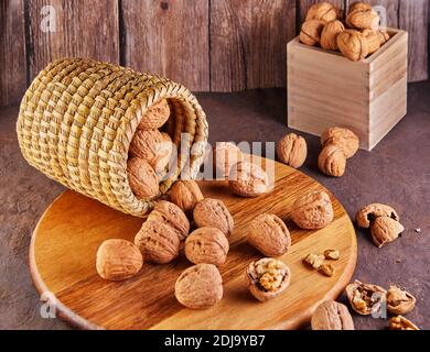 Walnuts in a wicker basket, whole and finely chopped, next to the filling and shells on a wooden background. Home storage of winter preparations Stock Photo