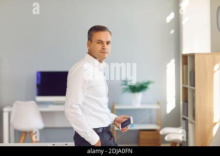 Businessman with a phone in his hands standing in the office and looking at the camera. Stock Photo