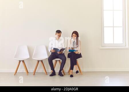 Two candidates with documents in their hands are sitting on chairs waiting for an interview. Stock Photo