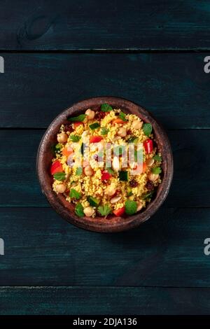 Vegetarian couscous salad with vegetables and herbs, overhead shot on a dark blue wooden background with a place for text Stock Photo
