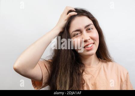 Dandruff and lice. Portrait of a young Caucasian brunette woman in a beige t-shirt, who strongly scratches her head with her hand. Copy space. White b Stock Photo