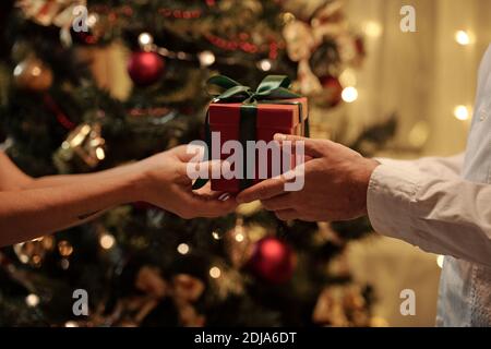 Close-up of unrecognizable woman giving red box wrapped in green ribbon while congratulating boyfriend on Christmas Stock Photo