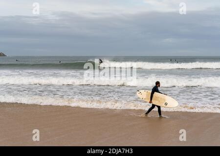 Baleal, Beira Litoral - Portugal - 13 December 2020: surfer walking on the beach at Baleal and watching other surfers catching waves Stock Photo