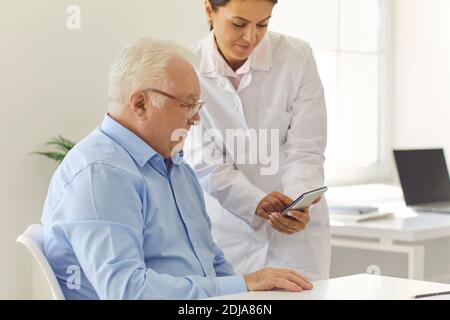 Nurse teaches old man to use phone app for setting medication reminder or tracking health indicators Stock Photo