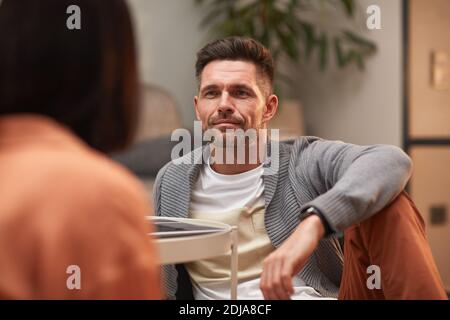 Portrait of handsome mature man looking at wife while sitting on floor in modern apartment and enjoying evening together, copy space Stock Photo