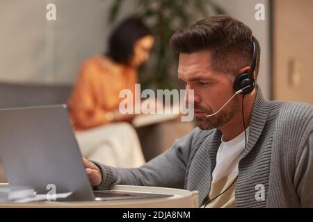 Portrait of mature man wearing headset and looking at laptop during online meeting while working from home, copy space Stock Photo