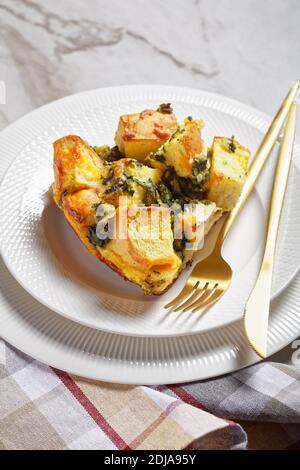 Strata or italian breakfast casserole of spinach, cheese and soaked overnight cubed bread baked with mustard on a white plate with golden cutlery on w Stock Photo