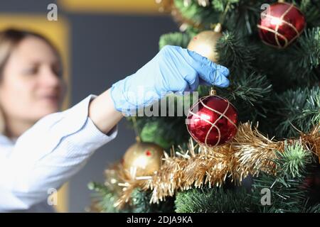Woman in protective rubber gloves hanging ball on Christmas tree closeup Stock Photo