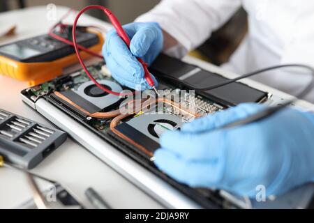 Professional repairman holding red tester in rubber gloves over laptop closeup Stock Photo