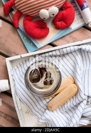 Summer breakfast scene with a couple of ladyfingers and a dark coffee cup on a wooden tray. A stuffed animal crab is enjoying the view. Stock Photo
