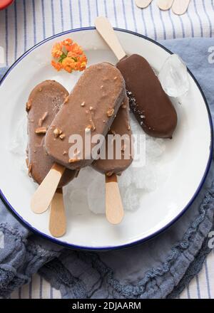 Four chocolate ice creams on a dish full of ice cubes. Three on a pile and the black one isolated. Stock Photo