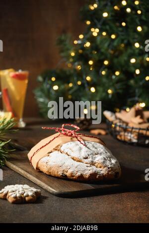 Homemade festive stollen on dark table in front of the Cristmas tree. Close up. Holiday Xmas food. Stock Photo