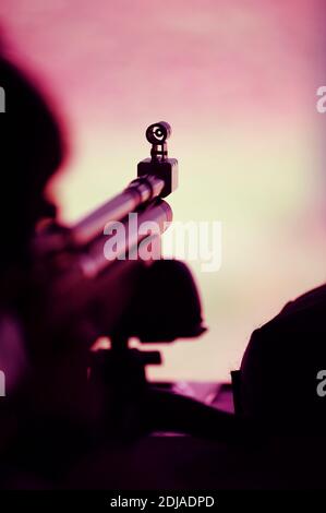 Sniper with rifle on tripod takes aim, ready to shoot. Theatre of war. Stock Photo