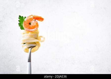 Fork with pasta and shrimp on white background, copy space. Fettuccine pasta with cream alfredo sauce and shrimp on fork close up. Stock Photo