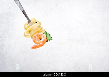 Fork with pasta and shrimp on white background, copy space. Fettuccine pasta with cream alfredo sauce and shrimp on fork close up. Stock Photo