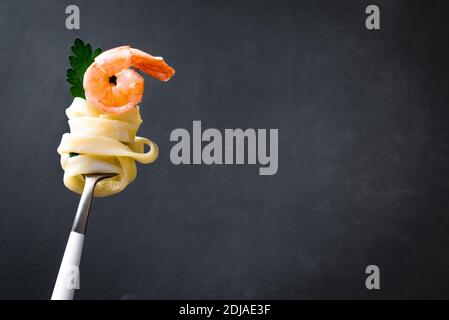 Fork with pasta and shrimp on dark background, copy space. Fettuccine pasta with cream alfredo sauce and shrimp on fork close up. Stock Photo