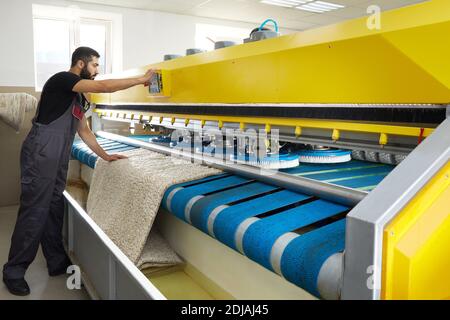 Man operating carpet automatic washing machine in professional laundry service Stock Photo