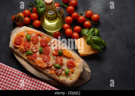 Flatbread pizza garnished with fresh cherry tomatoes,basil,cheese and olive oil on wooden pizza board. Dark background Stock Photo