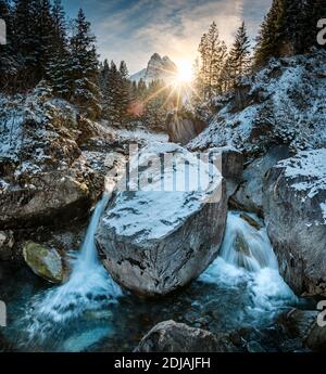 winter sun shining through the forest an wetterhorn over Rychenbach creek in Rosenlaui Valley Stock Photo