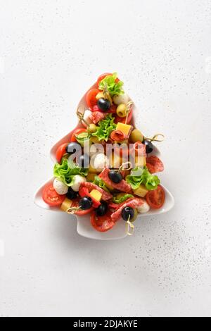 Holiday canapes in plate shaped of Christmas tree for festive Xmas party on white table. View from above. Vertical format. Stock Photo