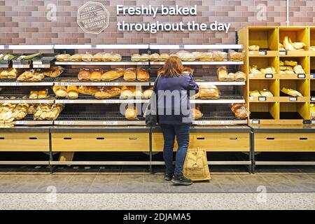 Back view of customer shopping for bread at Tesco supermarket in store bakery selection shelves below sign for freshly baked all day London England UK Stock Photo