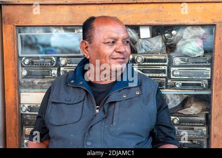 Jamnagar, Gujarat, India - December 2018: Candid portrait of a bald Indian shopkeeper sitting outside his hardware store. Stock Photo