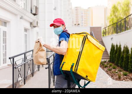 Portrait of a cheerful delivery man standing with yellow thermo backpack for food delivery on the street outdoors Stock Photo