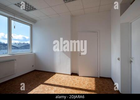 Modern interior of empty office room. White walls and door. Huge window. Sunny day. Stock Photo