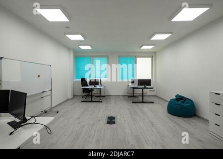 Modern light interior of spacious office room. Computers on tables. Marker board. Cozy beanbag chair. Stock Photo