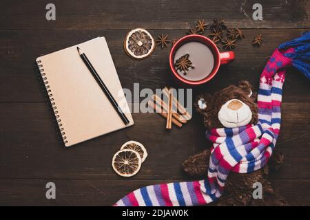 red ceramic cup with cocoa, notepad with blank sheets and brown teddy bear toy on a wooden table, top view Stock Photo