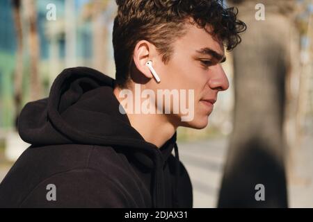 Close up handsome man listening music in wireless earphones. Attractive guy resting after workout outdoor Stock Photo