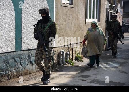 Kashmiri woman walks past of patrolling Indian troopers near site of attack in Srinagar.A policeman was killed after unknown gunmen fired at him at the residence of political party leader Parvaiz Bhat in the Natipora area of the Srinagar city, Police officials said. Stock Photo
