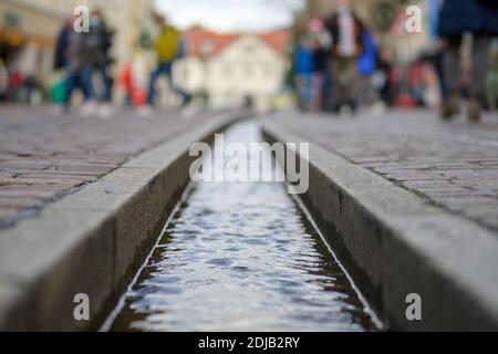 The Freiburg Bächle water runnel in close-up and selective focus ground level shot with pedestrians walking by in the street Stock Photo