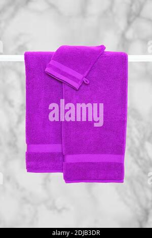 Hanging towels. Closeup of violet pink soft terry bath towels hang on a clothes rail in front of abstract blurred bright gray bath background. Stock Photo
