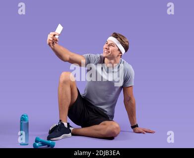 Full length portrait of positive young guy taking selfie with smartphone after training on violet studio background Stock Photo