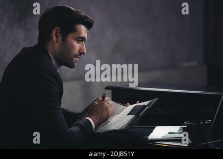 Businessman writes in a notebook while sitting at a desk, dark tone Stock Photo