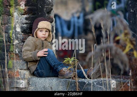 Cute child, posing in a ruin brick house, sitting on a window shield, autumn time Stock Photo