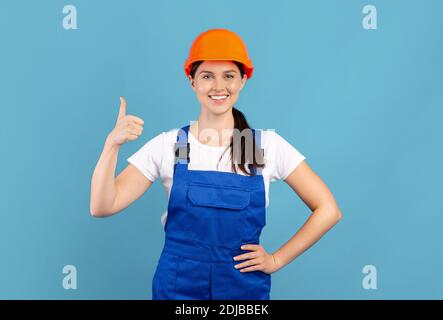 Portrait Of Young Handywoman Lady In Hardhat And Coveralls Showing Thumb Up Stock Photo