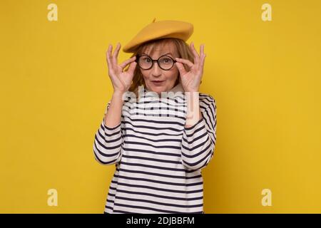 Middle age woman in yellow hat and glasses smiling looking at the camera. Positive person. Stock Photo