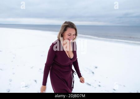 Curvy girl in the burgundy dress on the background of the winter sea. Portrait of a woman having fun on sea coast , windy weather, cold atmospheric im Stock Photo